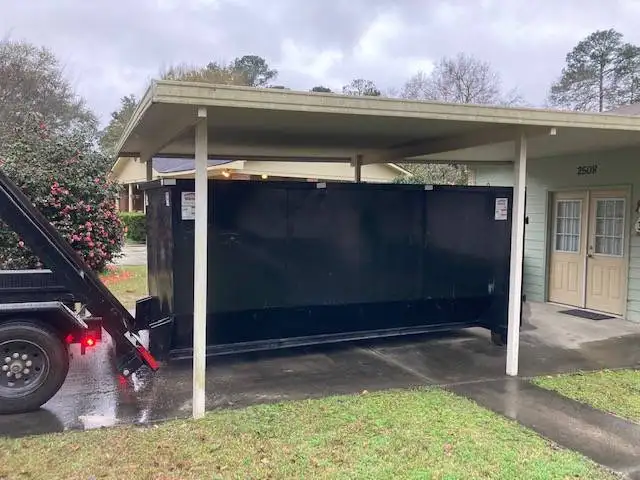 A photo of a black 20 yard dumpster rental being delivered to a house.